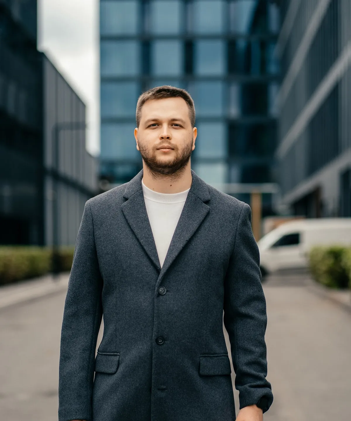 Богдан Щербаков у темно-сірому пальті стоїть на вулиці між скляними бізнес-центрами