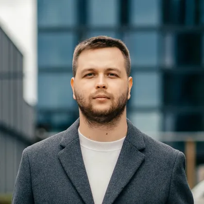 Богдан Щербаков у сірому пальті на тлі скляного бізнес-центру